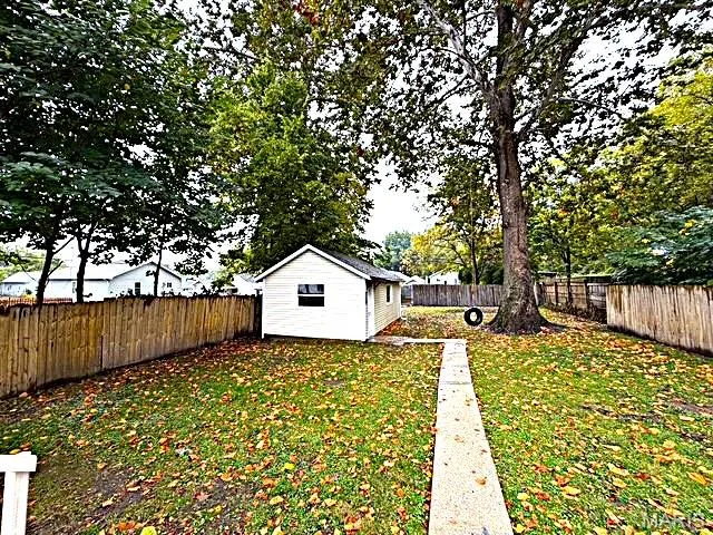 Backyard featuring a detached storage structure, concrete walkway, mature trees, and wood fencing — 529 Emmons Avenue, St Charles, MO 63301