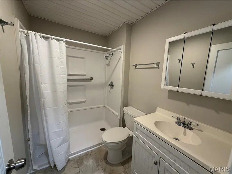 Full bathroom featuring a white vanity cabinet with an integrated sink, tri-fold mirrored medicine cabinet, neutral-tone tile flooring, and a shower-tub combination with built-in shelving — 529 Emmons Avenue, St Charles, MO 63301