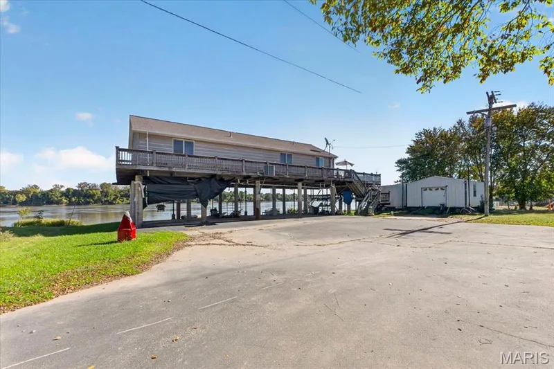 Stilt-constructed residence featuring a wood-rail wrap-around deck, paved driveway, and detached storage structure located on a waterfront lot — 69 Weule Boat Harbor, St Charles, MO 63301