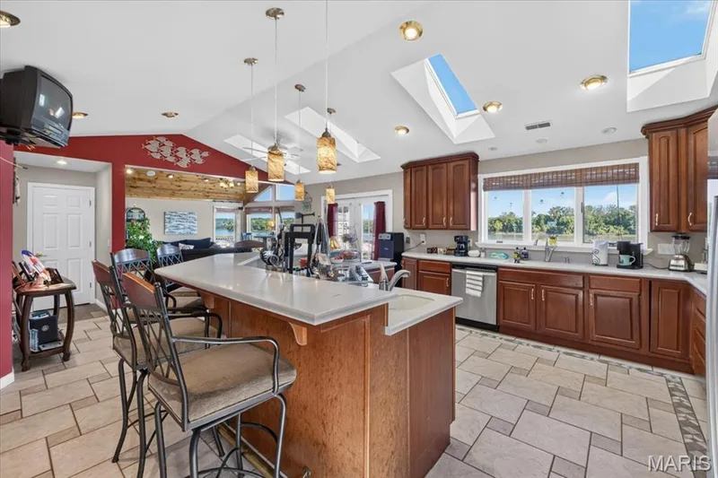 Kitchen featuring wood cabinetry, solid surface countertops, a center island with pendant lighting, stone-tile flooring, and multiple skylights — 69 Weule Boat Harbor, St Charles, MO 63301