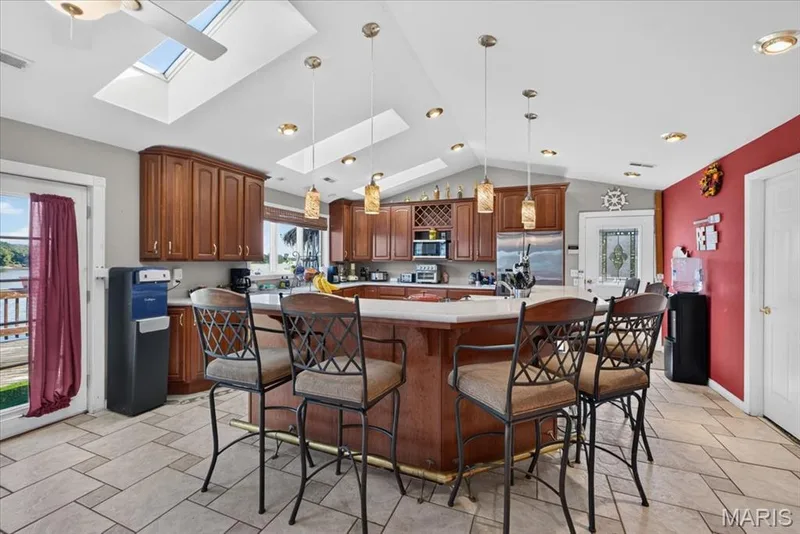 Kitchen featuring wood cabinetry, a central island with countertop seating, stone-style tile flooring, recessed lighting, and multiple skylights — 69 Weule Boat Harbor, St Charles, MO 63301