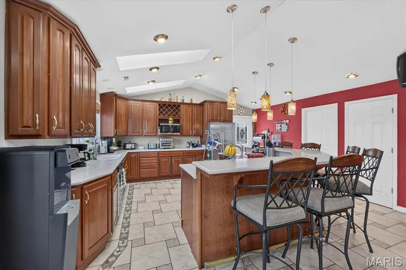 Kitchen featuring wooden cabinetry, integrated wine storage, an island with countertop seating, tiled flooring with decorative inlay, and skylights — 69 Weule Boat Harbor, St Charles, MO 63301