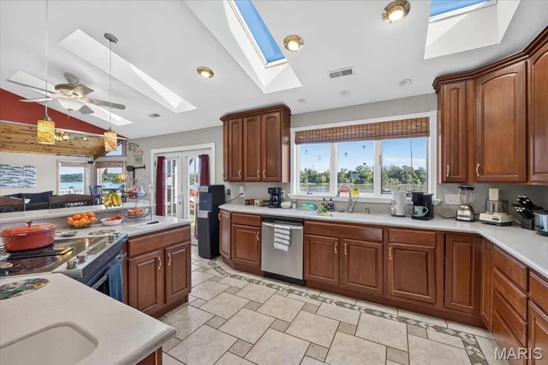 Kitchen featuring stained wood cabinetry, stone-finish countertops, tile flooring with decorative inlay, stainless steel appliances, and dual skylights — 69 Weule Boat Harbor, St Charles, MO 63301