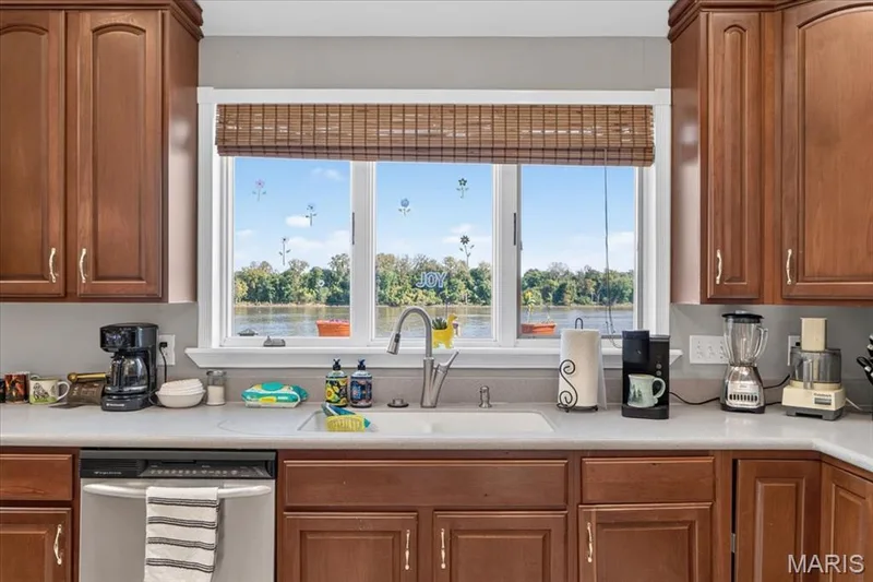 Kitchen featuring wood cabinetry, solid-surface countertops, a white undermount sink with a gooseneck faucet, stainless steel dishwasher, and a large window with water scenery — 69 Weule Boat Harbor, St Charles, MO 63301