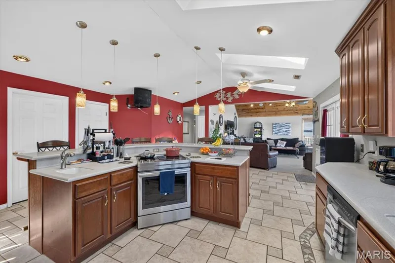 Kitchen featuring wood cabinetry, stone-finish countertops, stainless steel range, tiled flooring, and dual skylights — 69 Weule Boat Harbor, St Charles, MO 63301