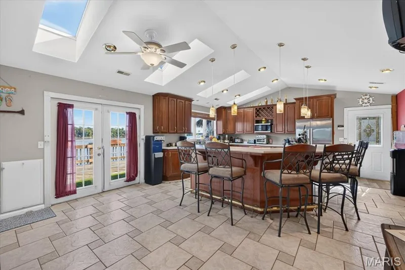 Kitchen featuring wooden cabinetry, a tiered island with integrated seating, stone-tile flooring, vaulted ceilings with multiple skylights, and double-glass paneled doors — 69 Weule Boat Harbor, St Charles, MO 63301