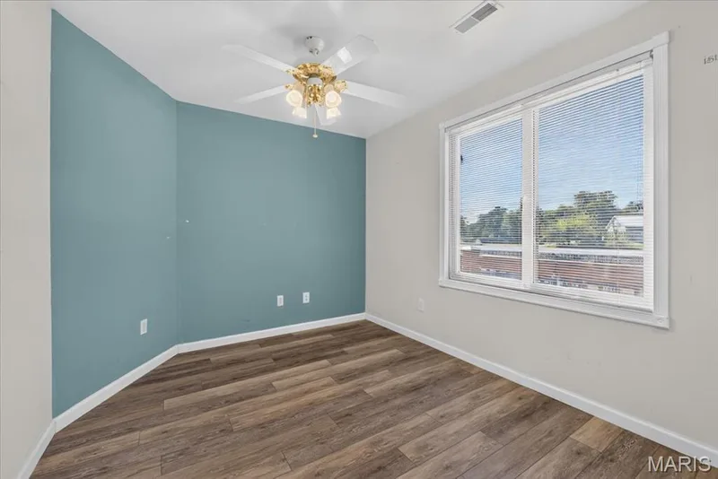 Room featuring wood-finish flooring, a blue accent wall, a white ceiling fan with integrated light fixture, and a large window with horizontal blinds — 69 Weule Boat Harbor, St Charles, MO 63301