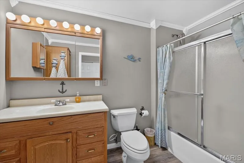 Bathroom featuring a wood-tone vanity, solid surface countertop with an integrated sink, multi-bulb vanity light, and a tub-shower combination with a sliding glass door enclosure — 69 Weule Boat Harbor, St Charles, MO 63301