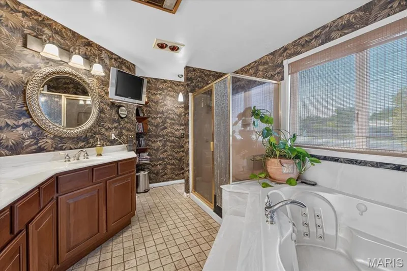 Bathroom featuring a jetted corner tub, separate glass-enclosed shower, wood vanity with a stone countertop, and circular wall-mounted mirror — 69 Weule Boat Harbor, St Charles, MO 63301