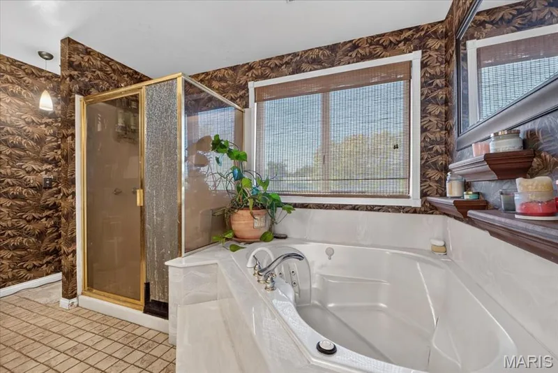 Corner soaking tub with integrated deck, glass-enclosed shower with gold-tone frame, patterned wallcovering, and built-in wooden shelving — 69 Weule Boat Harbor, St Charles, MO 63301