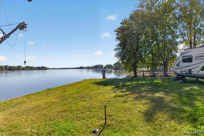 Waterfront property featuring an open grass lawn, mature trees, and a fixed metal boat lift — 69 Weule Boat Harbor, St Charles, MO 63301
