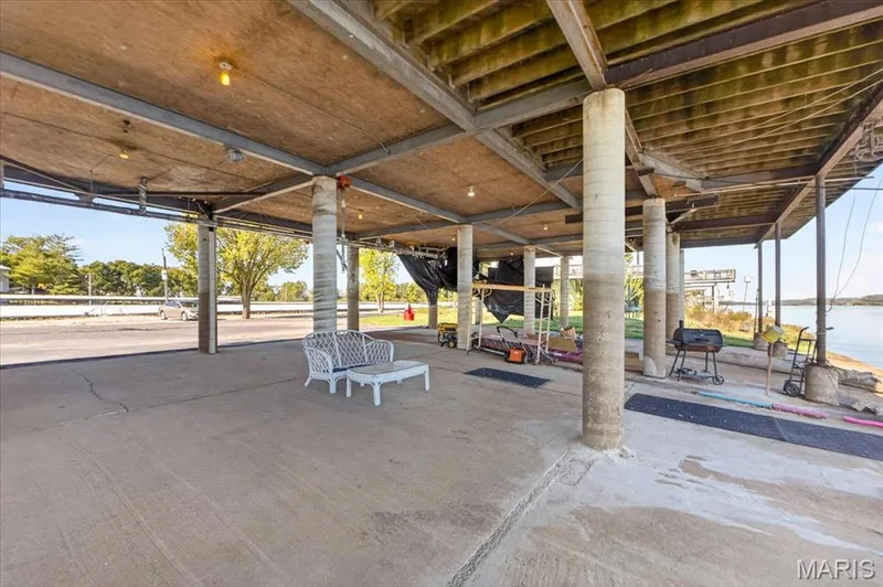 Covered lower-level patio featuring a concrete floor, cylindrical structural pillars, exposed wood ceiling joists, and direct waterfront access — 69 Weule Boat Harbor, St Charles, MO 63301