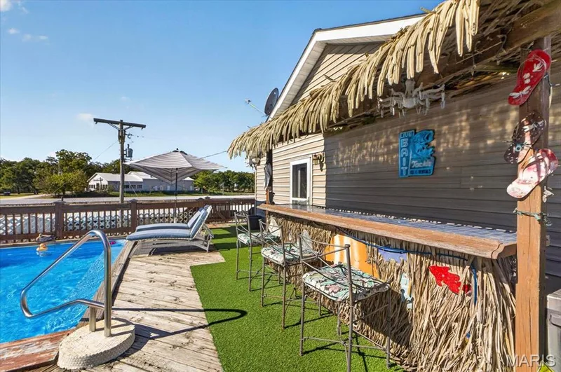 Outdoor entertainment area featuring an in-ground swimming pool, wood-plank decking, synthetic turf surfacing, and a built-in tiki-style bar with a thatched roof — 69 Weule Boat Harbor, St Charles, MO 63301