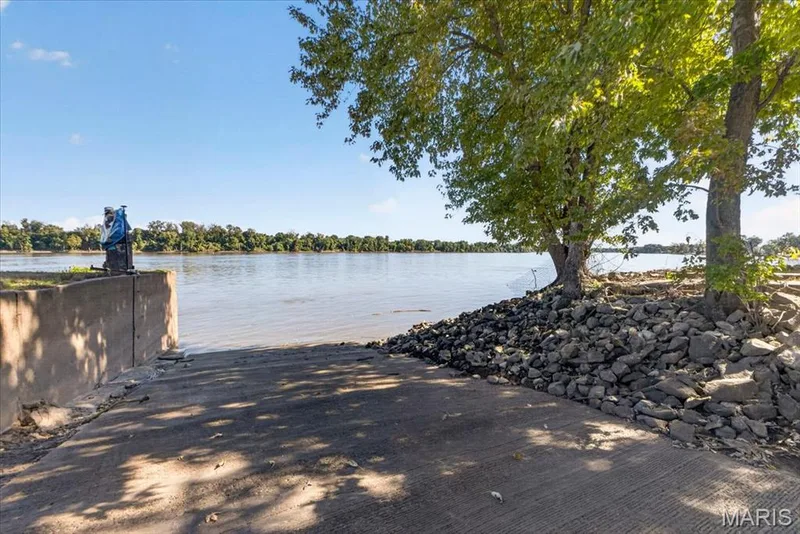 Concrete boat ramp featuring a stone-lined shoreline, retaining wall, and mature trees with direct water access — 69 Weule Boat Harbor, St Charles, MO 63301