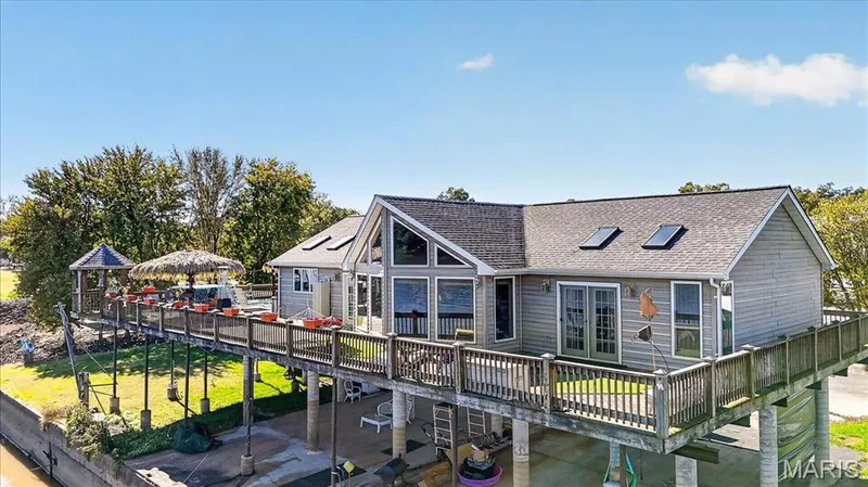 Elevated residence featuring horizontal siding, a gabled roofline with integrated skylights, expansive wraparound deck with wooden railing, and floor-to-ceiling windows — 69 Weule Boat Harbor, St Charles, MO 63301