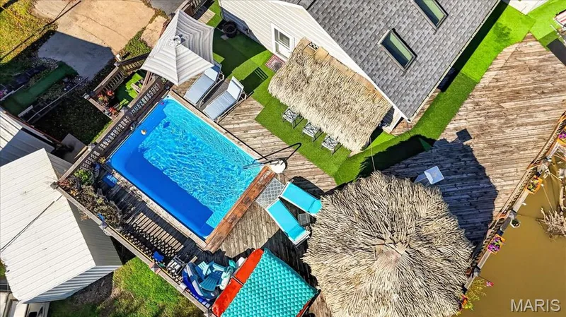 Outdoor living space featuring an in-ground swimming pool, wood-plank decking, synthetic turf lawn, and two thatched-roof structures — 69 Weule Boat Harbor, St Charles, MO 63301