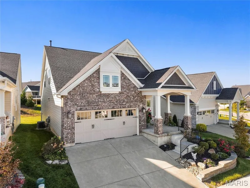 Multi-level exterior featuring a brick and horizontal lap siding façade, gabled rooflines, a multi-car garage with overhead windows, and a covered front entry with stone-clad pillars — 17028 Fire Glow Drive, Wildwood, MO 63011