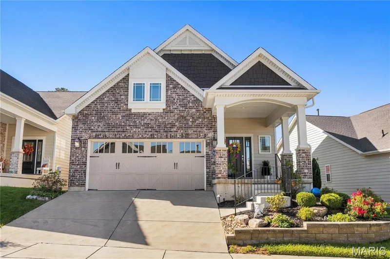 Multi-gabled exterior featuring a brick and composite siding facade, two-car garage with decorative hardware, and a covered front porch with arched supports and stone-base columns — 17028 Fire Glow Drive, Wildwood, MO 63011