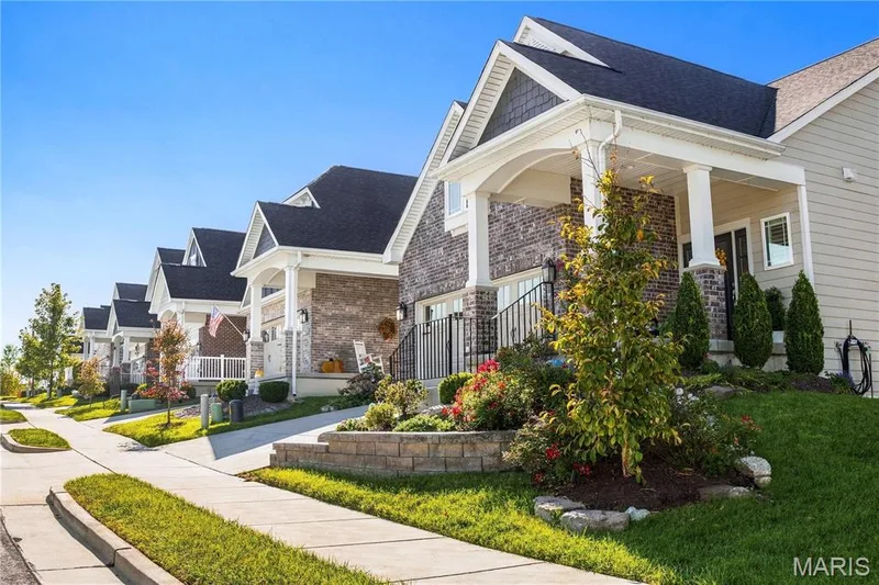 Exterior view featuring a masonry and lap siding façade, covered front porch with columns, shingle roof, and segmented retaining wall landscaping — 17028 Fire Glow Drive, Wildwood, MO 63011