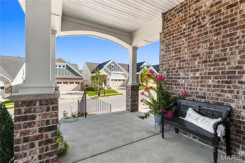 Covered front porch featuring a brick facade, concrete flooring with a decorative finish, and structural columns with stone-accented bases — 17028 Fire Glow Drive, Wildwood, MO 63011