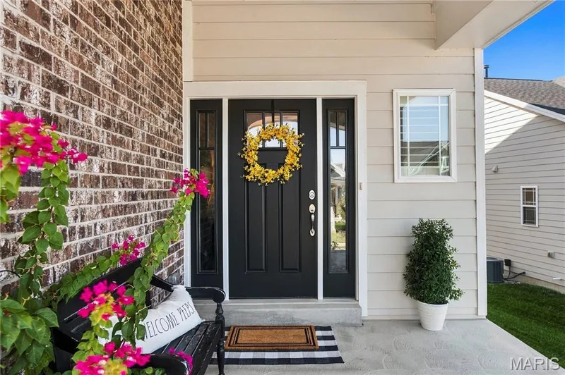 Covered concrete porch featuring a black front door with sidelights, horizontal lap siding, and a brick exterior veneer — 17028 Fire Glow Drive, Wildwood, MO 63011