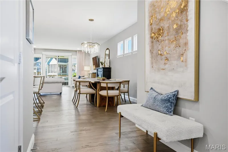 Open-concept interior featuring wood-finish flooring, a tiered crystal chandelier, transom windows, and a sliding glass door — 17028 Fire Glow Drive, Wildwood, MO 63011