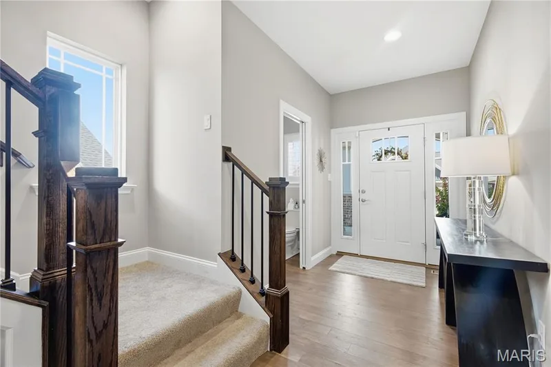 Foyer featuring wood-finish flooring, a white front door with glass sidelights, and a staircase with dark stained wood newel posts and metal balusters — 17028 Fire Glow Drive, Wildwood, MO 63011