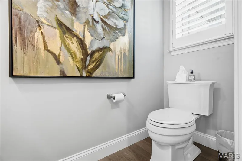 White ceramic toilet, wood-finish flooring, and window featuring plantation shutters — 17028 Fire Glow Drive, Wildwood, MO 63011