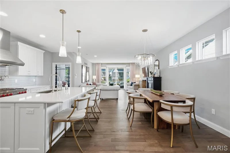 Open-concept kitchen and dining area featuring white shaker-style cabinetry, quartz countertops, wood-finish flooring, a stainless steel range hood, and tiered crystal chandelier lighting — 17028 Fire Glow Drive, Wildwood, MO 63011