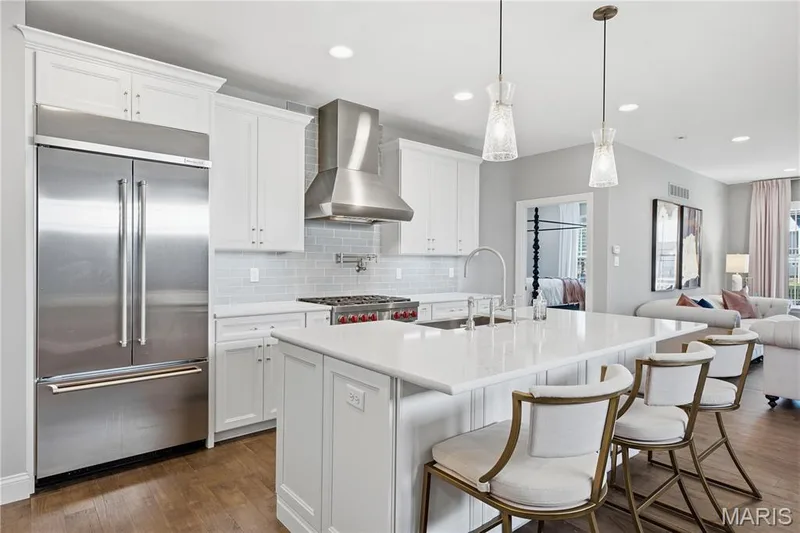 Kitchen featuring white cabinetry, professional-grade stainless steel appliances, subway tile backsplash, quartz countertops, and a central island with pendant lighting — 17028 Fire Glow Drive, Wildwood, MO 63011