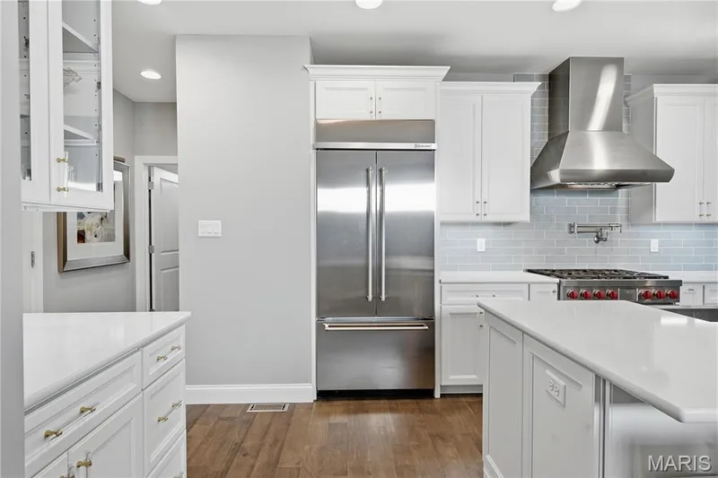Kitchen featuring white cabinetry, wood-finish flooring, light-colored stone-finish countertops, stainless steel appliances, and a subway tile backsplash — 17028 Fire Glow Drive, Wildwood, MO 63011