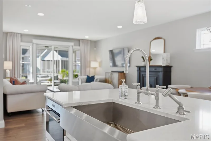 Kitchen island featuring a stone countertop, an integrated stainless steel farmhouse sink, and a multi-handle bridge faucet with a side sprayer — 17028 Fire Glow Drive, Wildwood, MO 63011