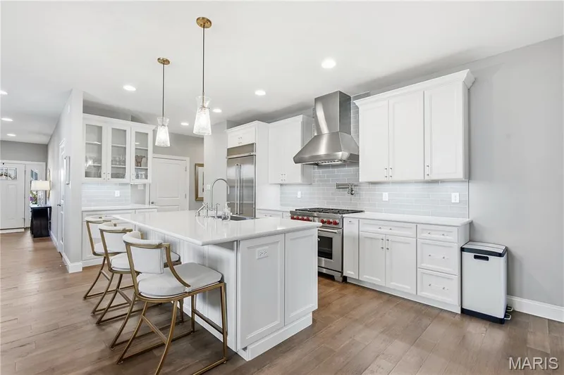 Kitchen featuring white shaker-style cabinetry, quartz countertops, stainless steel appliances, subway tile backsplash, and wood-finish flooring — 17028 Fire Glow Drive, Wildwood, MO 63011