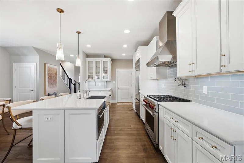 Kitchen featuring white shaker cabinetry, quartz countertops, a subway tile backsplash, wood-finish flooring, and a stainless steel professional-style range with a chimney hood — 17028 Fire Glow Drive, Wildwood, MO 63011