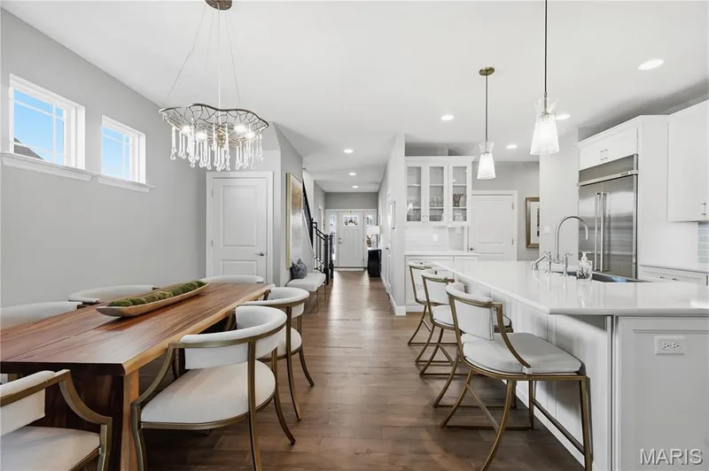 Open-concept kitchen featuring an expansive quartz-topped island, wood-finish flooring, built-in glass-front cabinetry, recessed lighting, and a prominent crystal chandelier — 17028 Fire Glow Drive, Wildwood, MO 63011