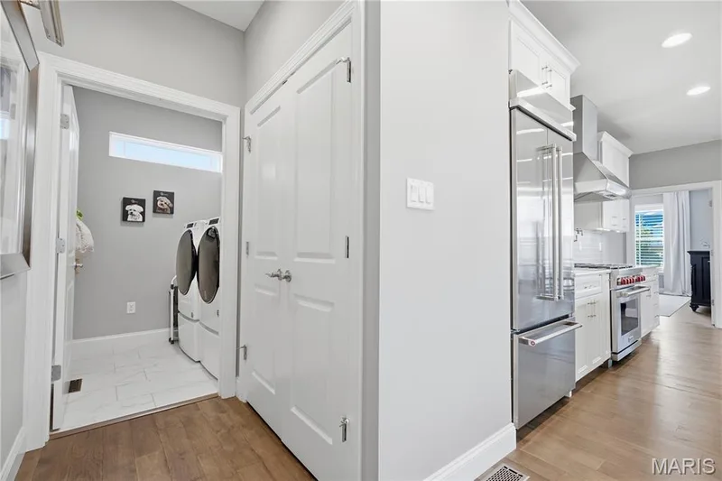 Kitchen featuring stainless steel appliances, white cabinetry, and wood-finish flooring, with a separate utility space containing white tile flooring and recessed lighting — 17028 Fire Glow Drive, Wildwood, MO 63011
