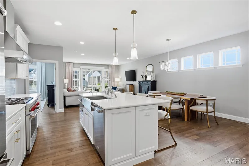 Open-concept kitchen featuring an expansive center island with a farmhouse sink, stainless steel range with a ventilation hood, wood-finish flooring, and recessed lighting — 17028 Fire Glow Drive, Wildwood, MO 63011