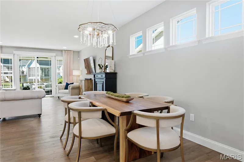 Open-concept interior featuring wood-finish flooring, a tiered crystal chandelier, and a series of transom windows — 17028 Fire Glow Drive, Wildwood, MO 63011