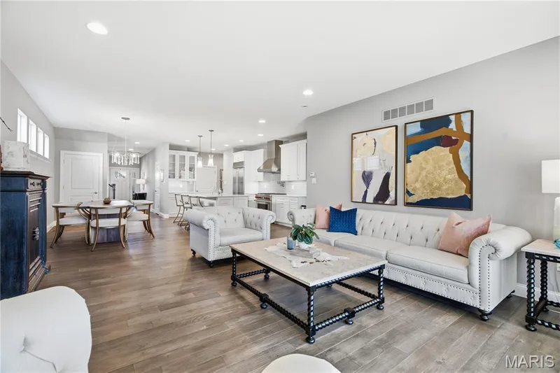 Open-concept living space featuring wood-finish flooring, recessed lighting, and kitchen with white cabinetry, stainless steel appliances, and a central island — 17028 Fire Glow Drive, Wildwood, MO 63011