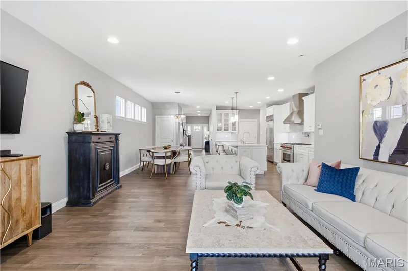 Open-concept floor plan featuring wood-finish flooring, recessed lighting, white cabinetry, a center kitchen island, and a stainless steel range hood — 17028 Fire Glow Drive, Wildwood, MO 63011