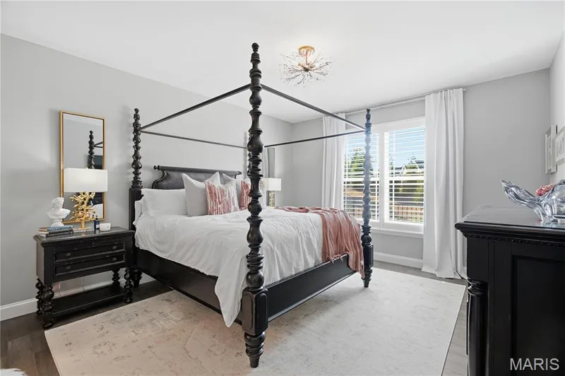 Bedroom featuring wood-finish flooring, multi-pane window with plantation shutters, and starburst-style ceiling light fixture — 17028 Fire Glow Drive, Wildwood, MO 63011
