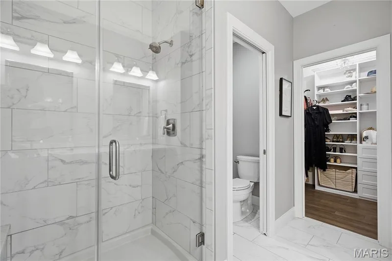 Walk-in shower featuring large-format stone-look tile walls and a glass enclosure, paired with a walk-in wardrobe with built-in custom shelving and wood-finish flooring — 17028 Fire Glow Drive, Wildwood, MO 63011