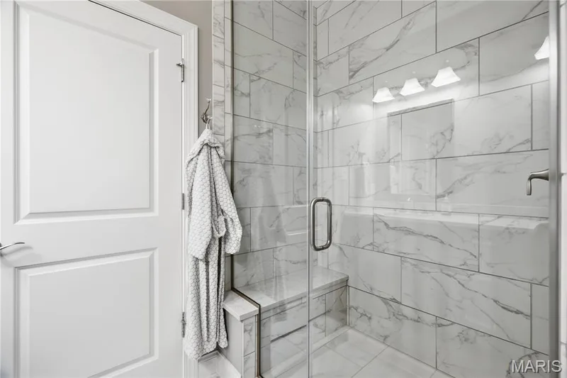 Walk-in shower featuring large-format stone-patterned wall tile, a built-in bench seat, frameless glass enclosure, and brushed nickel hardware — 17028 Fire Glow Drive, Wildwood, MO 63011