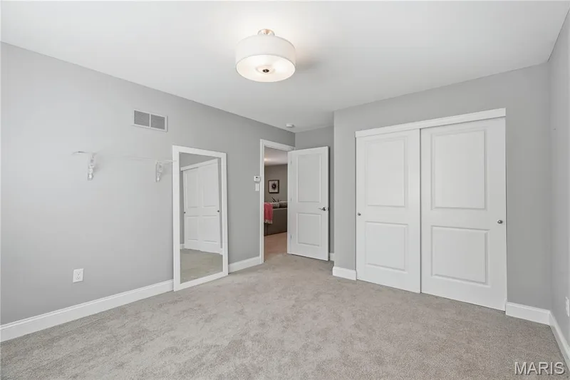 Room featuring wall-to-wall carpeting, a semi-flush mount drum ceiling light, a full-length wall-mounted mirror, and a double-door closet with raised-panel doors — 17028 Fire Glow Drive, Wildwood, MO 63011