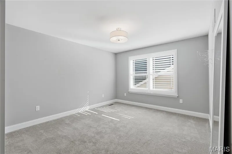 Neutral-toned interior room featuring wall-to-wall carpeting, white plantation shutters, and a central drum-style flush-mount light fixture — 17028 Fire Glow Drive, Wildwood, MO 63011