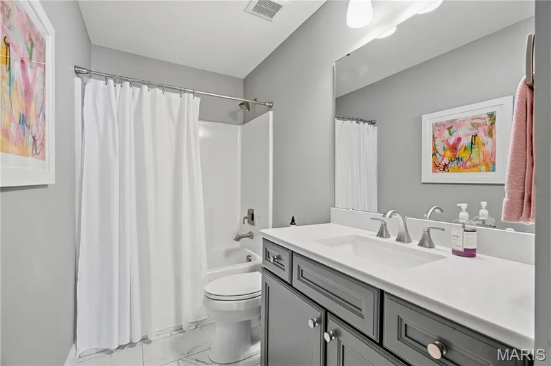 Bathroom featuring a vanity with dark gray cabinetry, a white stone countertop, an integrated rectangular sink, a large wall-mounted mirror, and a tub-shower combination with white surround — 17028 Fire Glow Drive, Wildwood, MO 63011