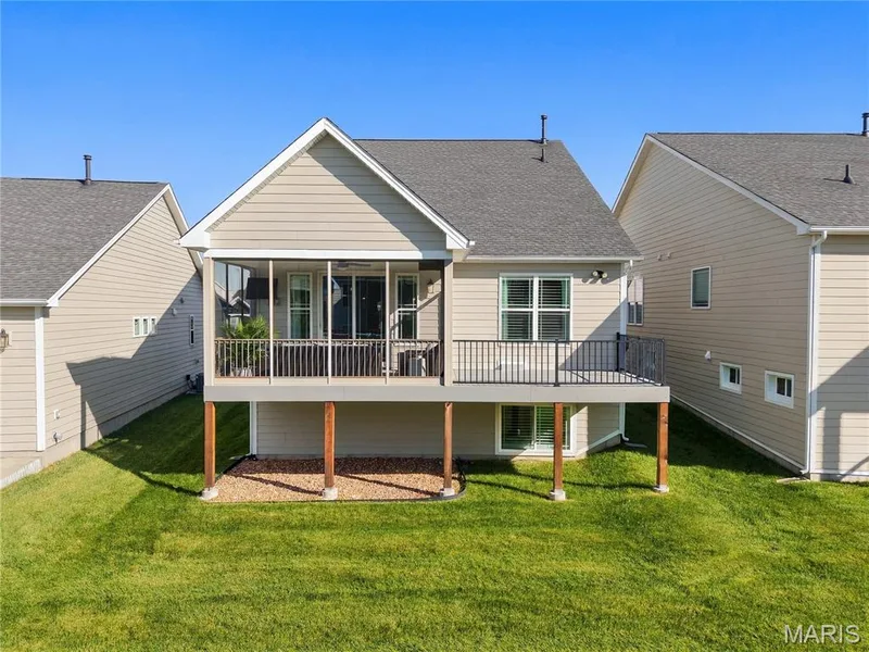 Rear elevation featuring a screened-in porch with metal railing, an elevated deck, and a gravel hardscape area — 17028 Fire Glow Drive, Wildwood, MO 63011