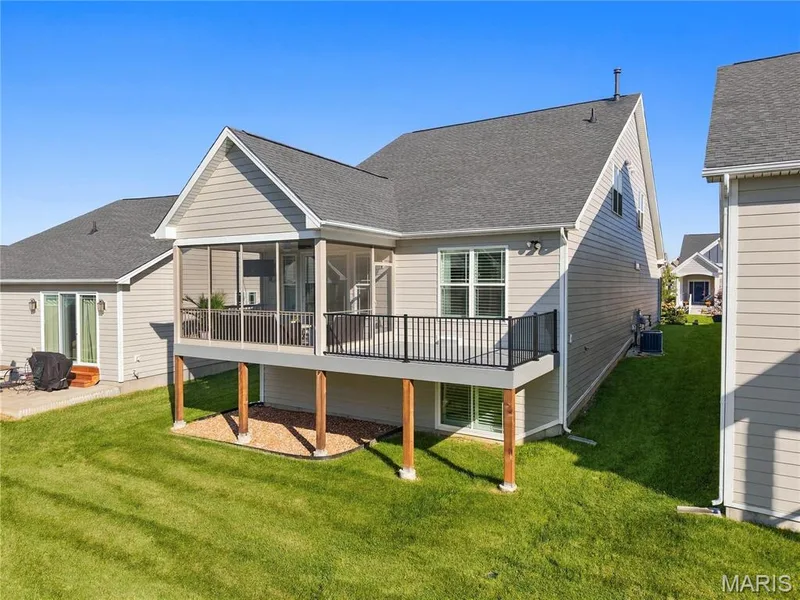 Rear elevation featuring horizontal lap siding, a screened-in porch with metal railing, a composite deck extension, and a ground-level stone-mulched patio area — 17028 Fire Glow Drive, Wildwood, MO 63011
