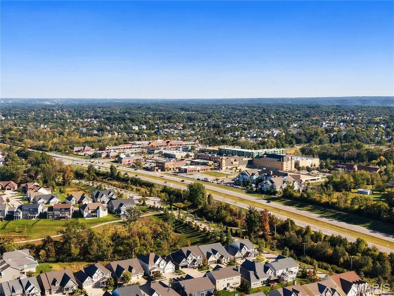 Aerial perspective of a residential neighborhood featuring expansive tree-lined surroundings, multi-story single-family dwellings, and proximity to regional infrastructure — 17028 Fire Glow Drive, Wildwood, MO 63011
