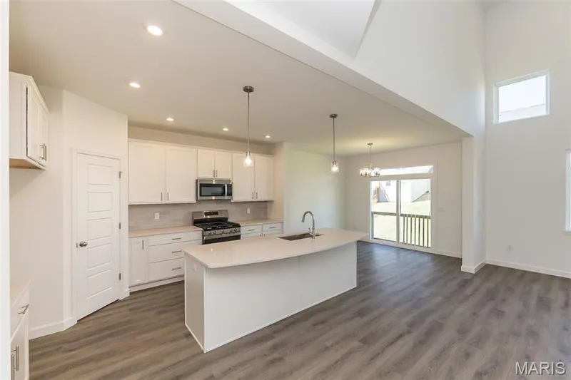 Kitchen featuring a kitchen island with sink, appliances with stainless steel finishes, hanging light fixtures, backsplash, and white cabinets — 717 Southerland Drive, O'Fallon, MO 63368